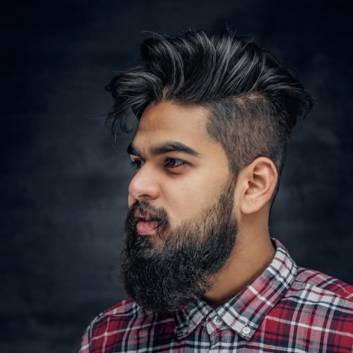 Attractive bearded Indian man in plaid fleece shirt over grey background.