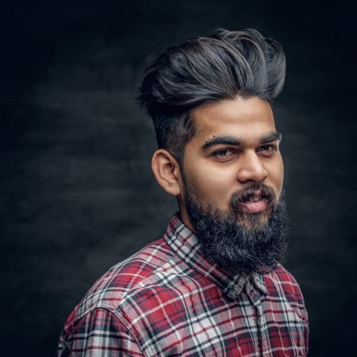 A handsome bearded Indian male dressed in a fleece shirt over grey vignette background.