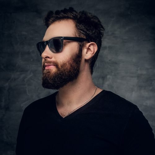 Stylish bearded male in sunglasses over grey background.